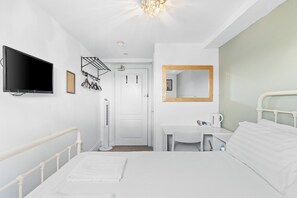 A hotel room with a bed, a desk, a chair, a TV, a mirror, and a door.