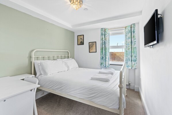 A bedroom with a bed, a bedside table, a television mounted on the wall, and a window with curtains.