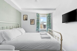 A bedroom with a bed, a flat-screen TV mounted on the wall, and a window with curtains.