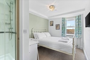 A bedroom with a bed, a shower, a television, and a window with curtains.