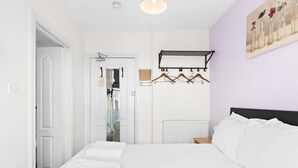 A bedroom with a bed, a coat rack, a radiator, and a door leading to another room. - Brighton Escape – Steps from Pier & The Lanes (Brighton and Hove)