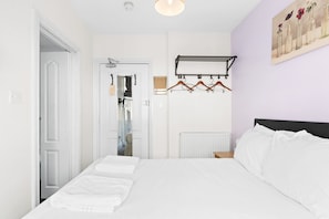 A bedroom with a bed, a coat rack, a radiator, and a door leading to another room.