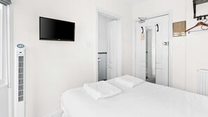 A hotel room with a bed, a television, a radiator, and a door leading to a bathroom.