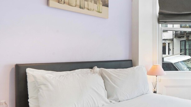 A bed with white bedding, a dark headboard, a wall-mounted light fixture, and a bottle of water on a nightstand.