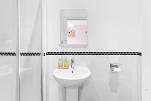 A bathroom with a white sink, a mirror, and a shower area. - Brighton Escape – Steps from Pier & The Lanes (Brighton and Hove)