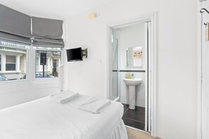 A hotel room with a bed, a TV mounted on the wall, a bathroom with a sink and mirror, and a view of the street through a window.