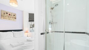 A hotel room with a bed, a glass-enclosed shower, and a painting on the wall.