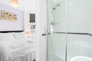 A hotel room with a bed, a glass-enclosed shower, and a painting on the wall.