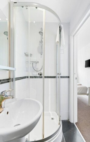A modern bathroom with a glass-enclosed shower, a white sink, and a tiled shower area.