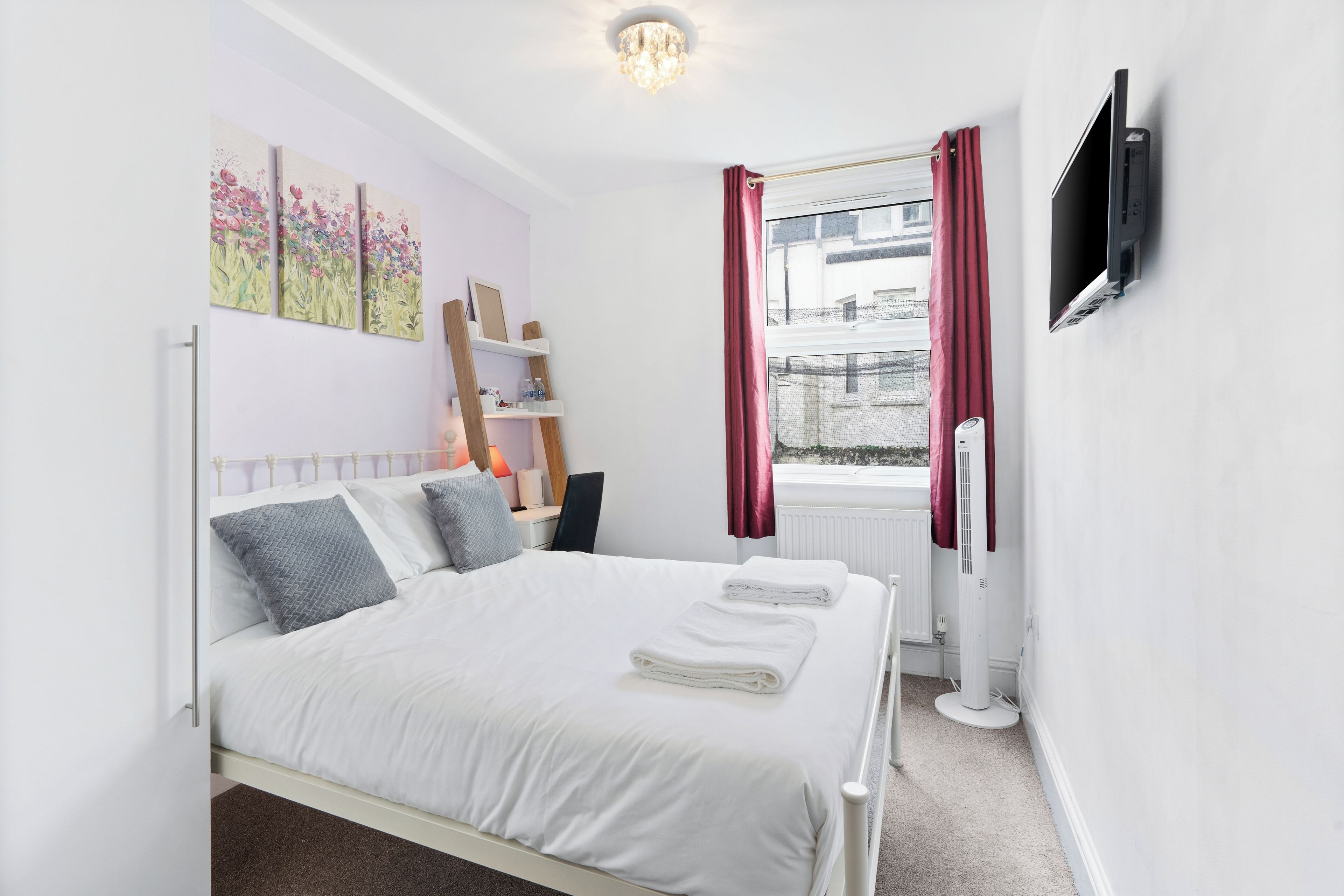 A bedroom with a bed, a TV, a radiator, and a window with curtains.