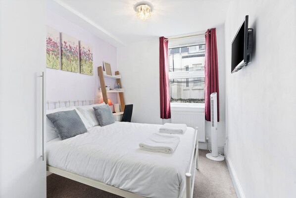 Une chambre à coucher avec un lit, une télévision, un radiateur et une fenêtre avec des rideaux.