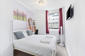 Un dormitorio con cama, televisión, radiador y ventana con cortinas.