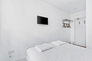 A minimalist hotel room with a bed, a flat-screen TV mounted on the wall, a coat rack with hangers, and a door with a handle. - Chic stay by the Sea: close to Shops & Bars (Brighton and Hove)