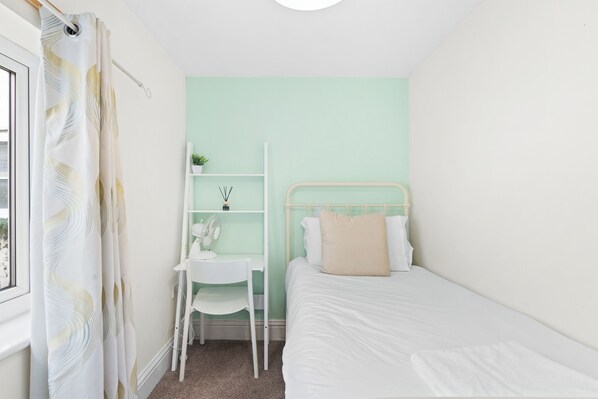 Une chambre à coucher avec un lit, un bureau avec une chaise, une étagère avec une plante et une fenêtre avec des rideaux.