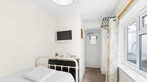 Une chambre à coucher comprenant un lit, une table de chevet, un téléviseur fixé au mur, une porte et une fenêtre avec des rideaux.