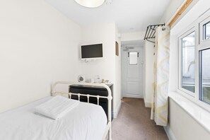 Une chambre à coucher comprenant un lit, une table de chevet, un téléviseur fixé au mur, une porte et une fenêtre avec des rideaux.