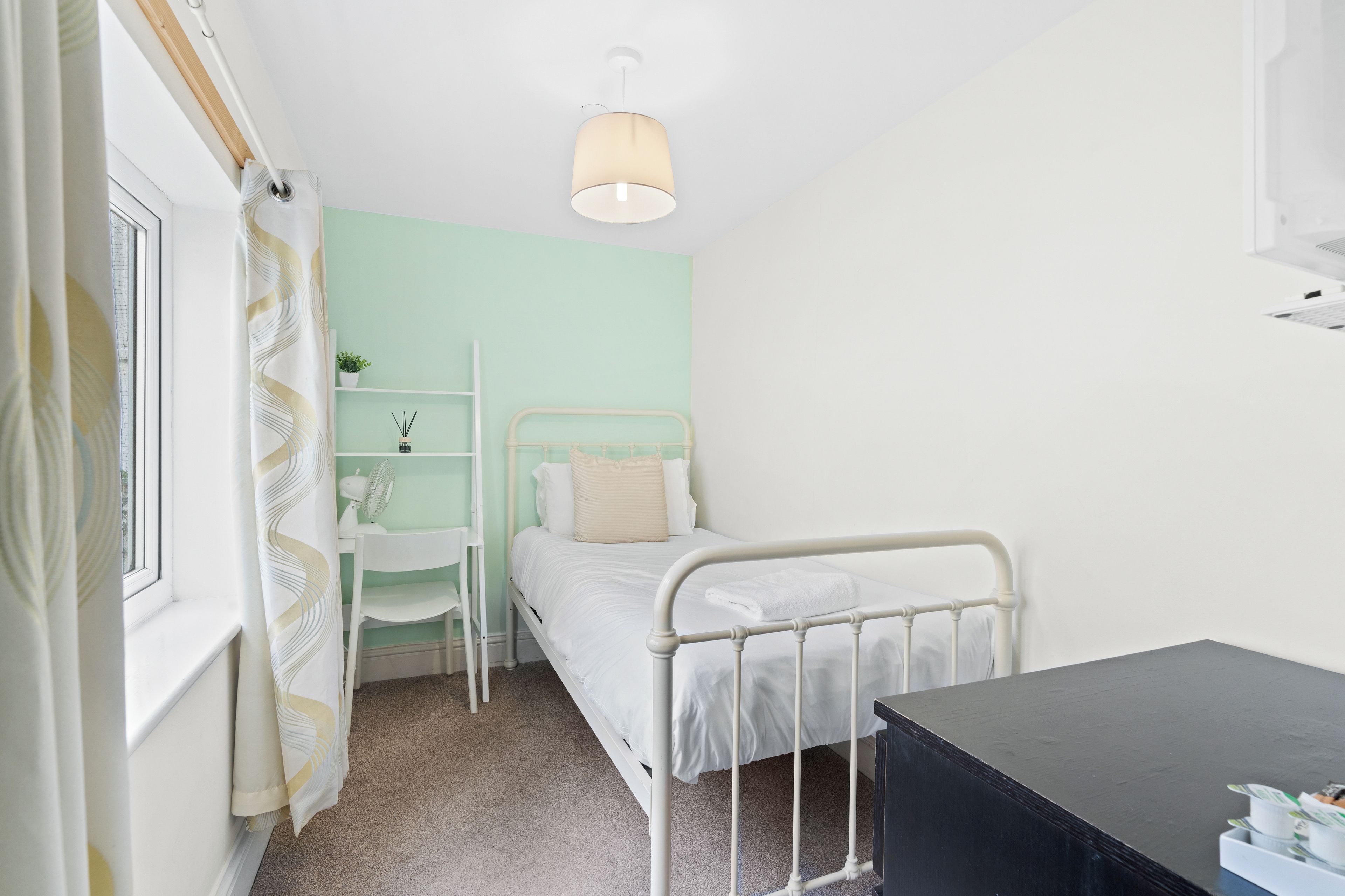 A small, neatly arranged bedroom with a single bed, a desk, and a chair.