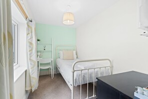 Quarto pequeno e bem organizado com uma cama de solteiro, uma escrivaninha e uma cadeira.