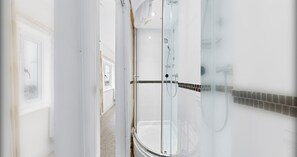 A modern bathroom with a glass-enclosed shower, white walls, and a tiled floor.