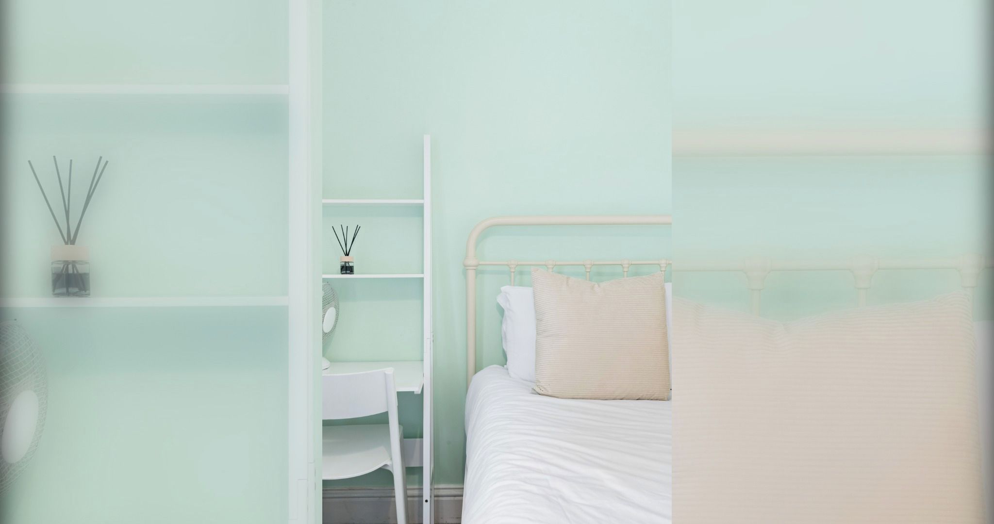 A bedroom with a bed, a white nightstand, and a shelf with a diffuser and a small mirror.