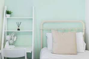 Une chambre à coucher avec un lit, une chaise blanche, une étagère blanche et une petite plante en pot.