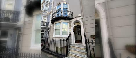 A corner building with a white facade, a black iron fence, and a small entrance with steps leading up to it.