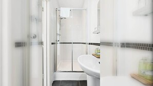 A modern bathroom with a glass shower enclosure, a white sink, and black-tiled walls. - Seaside Charm: Next to The Pier, Top Attractions (Brighton and Hove)
