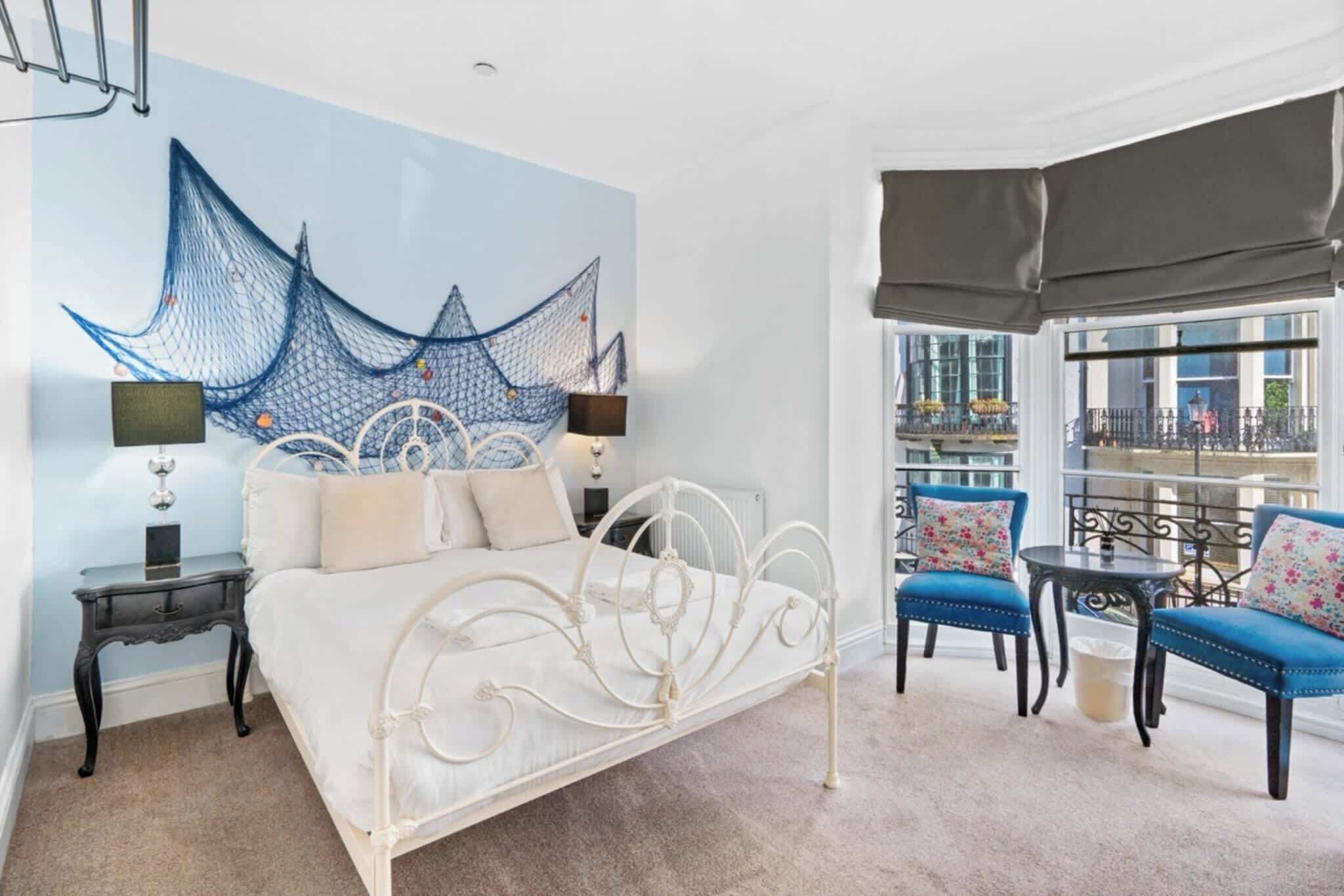 A bedroom with a bed, bedside tables, a large window with a view, and a balcony with seating.