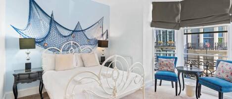 A bedroom with a bed, bedside tables, a large window with a view, and a balcony with seating.