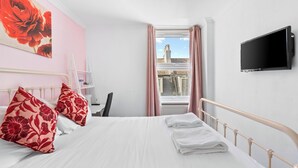 A hotel room with a bed, a TV, a window with curtains, and a view of buildings outside. - Brighton Bliss: Cozy Stay by the Pier & Marina (Brighton and Hove)
