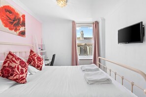 A hotel room with a bed, a TV, a window with curtains, and a view of buildings outside. - Brighton Bliss: Cozy Stay by the Pier & Marina (Brighton and Hove)