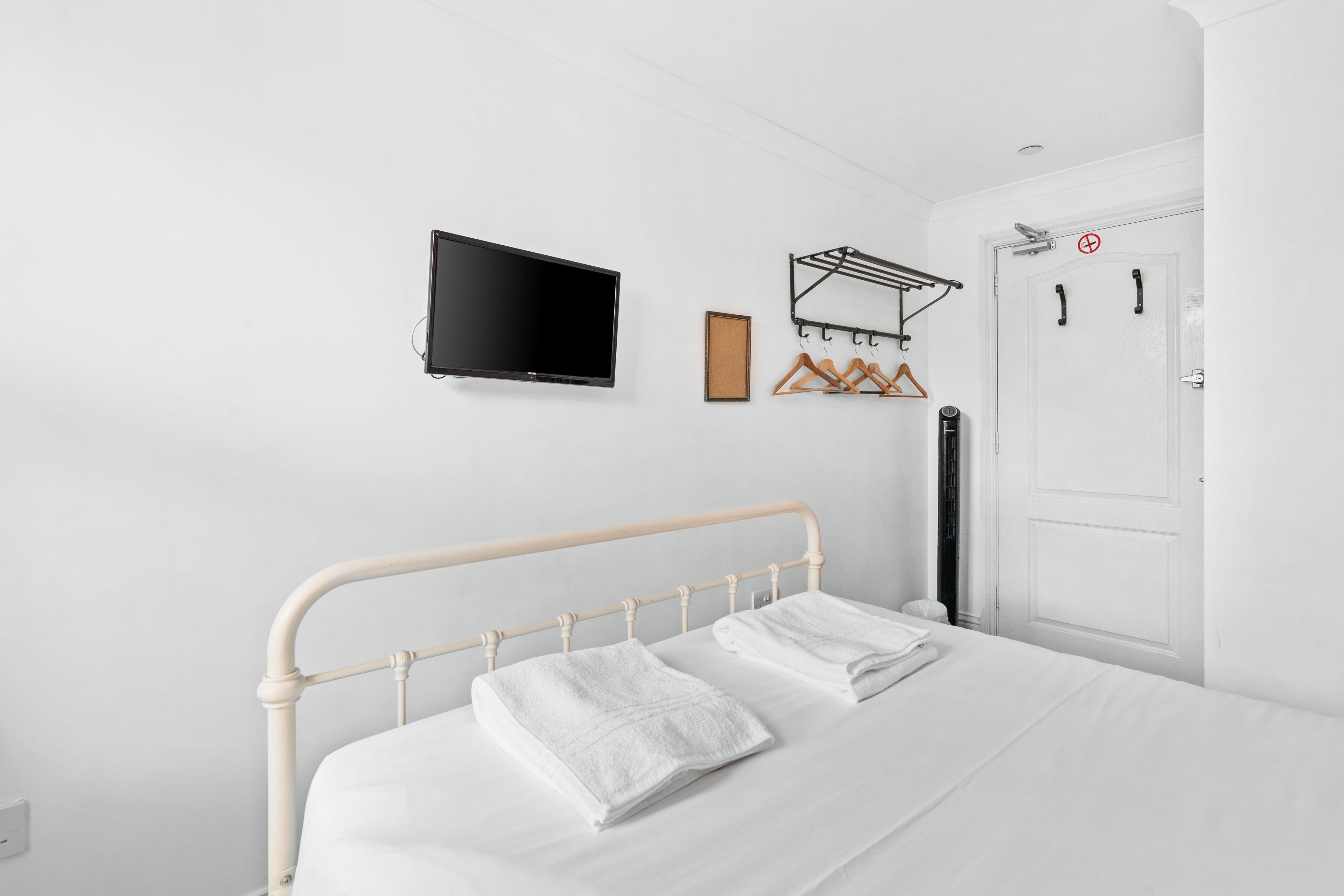 A bedroom with a bed, a television, a coat rack, and a door.