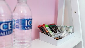 Ein weißes Regal mit einem weißen Behälter, der verschiedene Gegenstände enthält, darunter eine Wasserflasche, eine weiße Tasse und eine weiße Schachtel mit bunten Artikeln.
