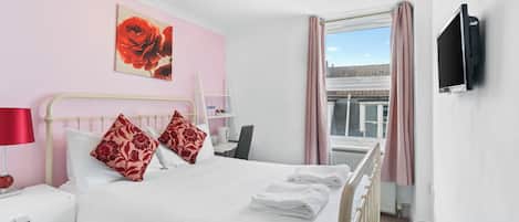 A hotel room with a bed, a TV mounted on the wall, a window with curtains, and a painting on the wall.