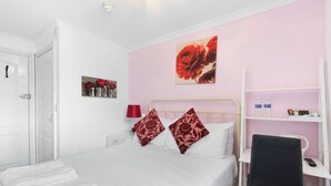 A hotel room with a bed, a desk, a chair, a shelf with toiletries, and a door. - Brighton Bliss: Cozy Stay by the Pier & Marina (Brighton and Hove)
