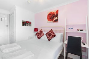 A hotel room with a bed, a desk, a chair, a shelf with toiletries, and a door. - Brighton Bliss: Cozy Stay by the Pier & Marina (Brighton and Hove)
