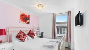 A hotel room with a bed, a TV mounted on the wall, a window with curtains, and a painting on the wall. - Brighton Bliss: Cozy Stay by the Pier & Marina (Brighton and Hove)