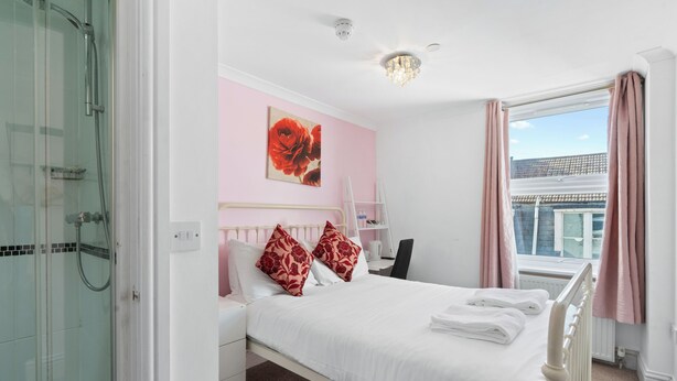 A hotel room with a bed, a shower, a window with curtains, and a view of buildings outside. - Brighton Bliss: Cozy Stay by the Pier & Marina (Brighton and Hove)