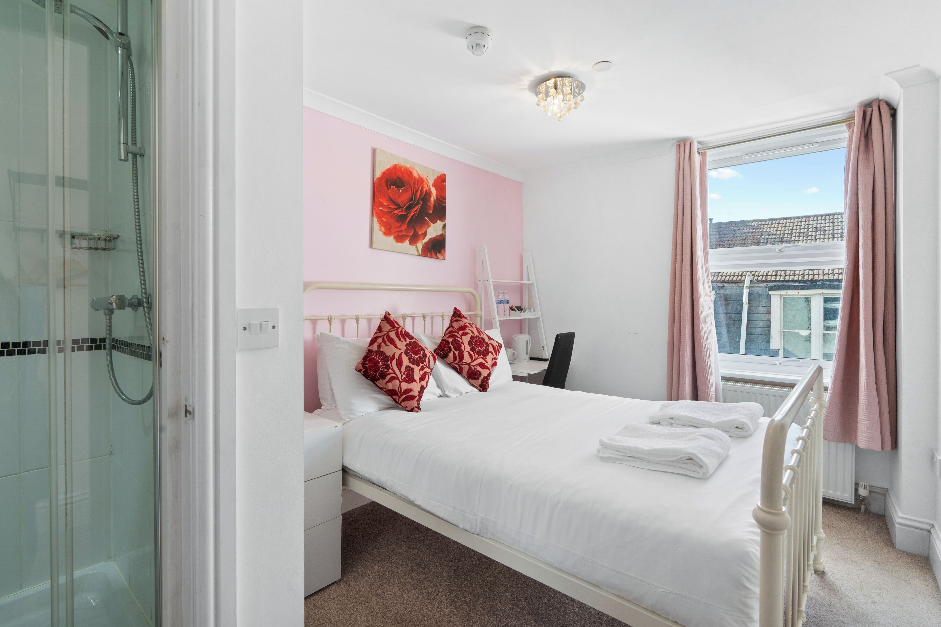 A hotel room with a bed, a shower, a window with curtains, and a view of buildings outside.