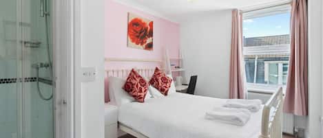 Una habitación de hotel con cama, ducha, ventana con cortinas y vistas a edificios.