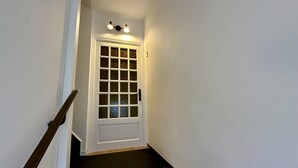A narrow staircase with a wooden handrail leading to a white door with a glass panel.