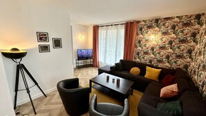 A living room with a sofa, coffee table, and a floor lamp. There is a television on a stand and a patterned wall.