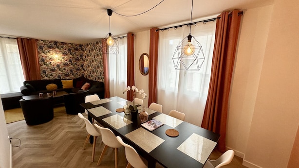 A modern dining area with a long table, white chairs, and geometric pendant lights.