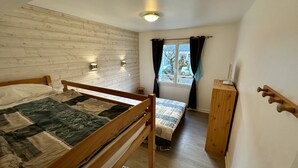 Una habitación pequeña y acogedora con una cama de madera, un escritorio y una ventana con cortinas.