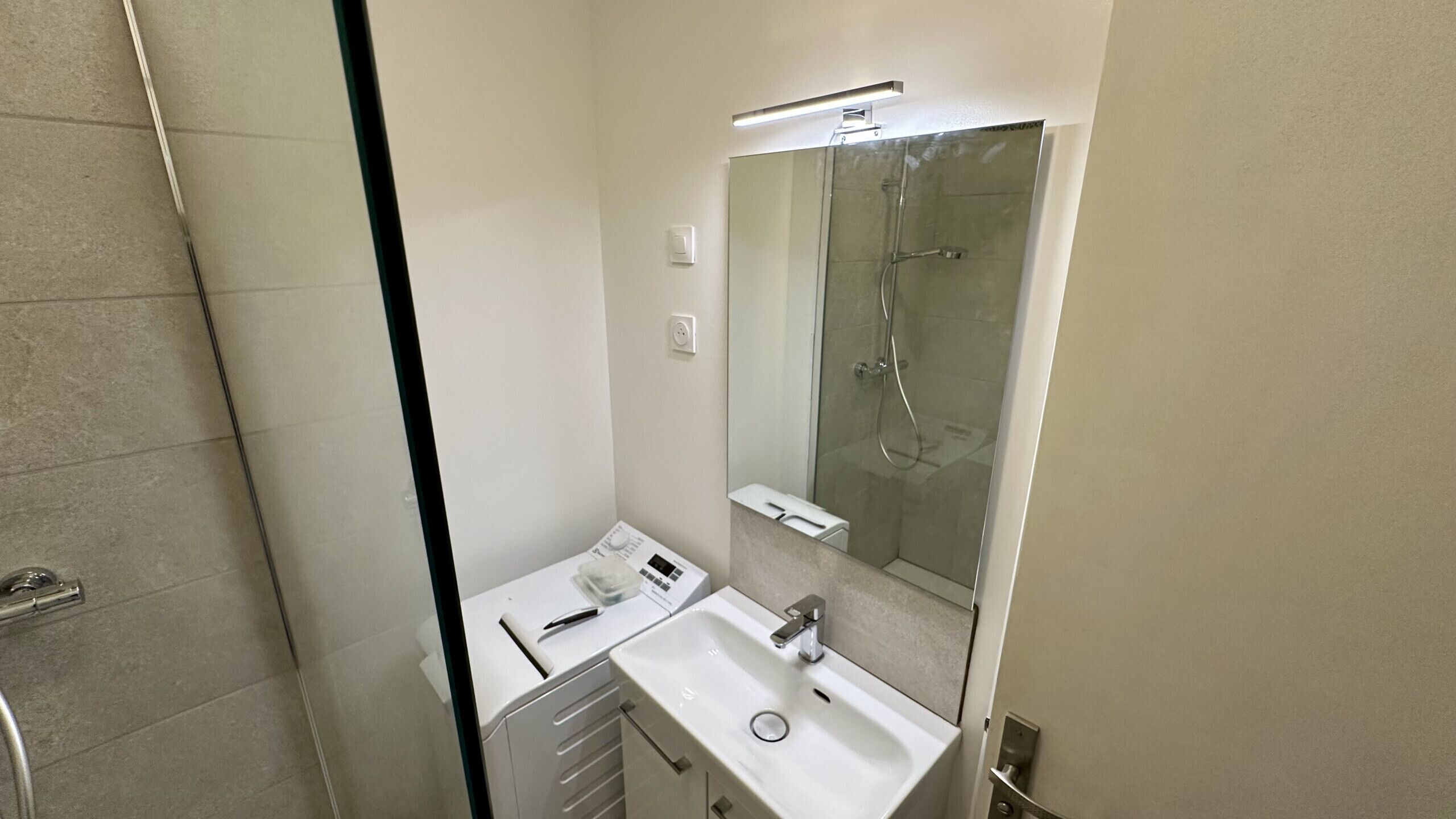 Uma casa de banho com lavatório branco, espelho e cabine de duche em vidro.