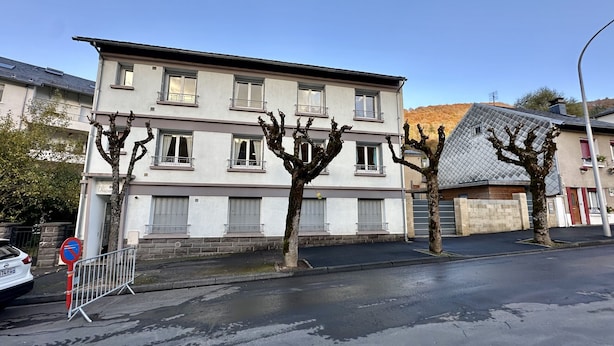 Un edificio residencial de varios pisos con balcones, una entrada con reja y un coche estacionado.