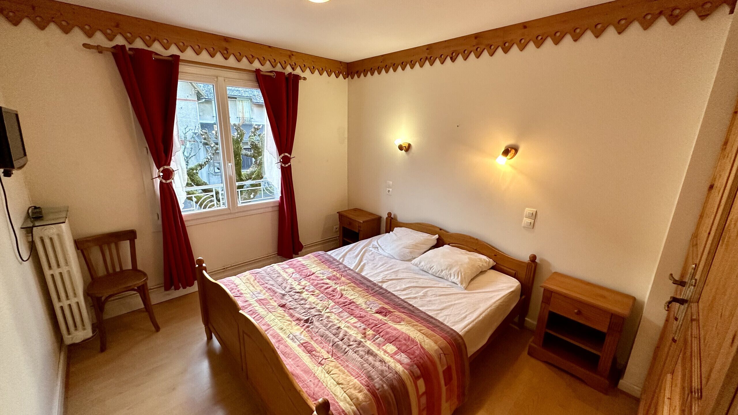 A bedroom with a bed, a chair, a radiator, and a window with curtains.