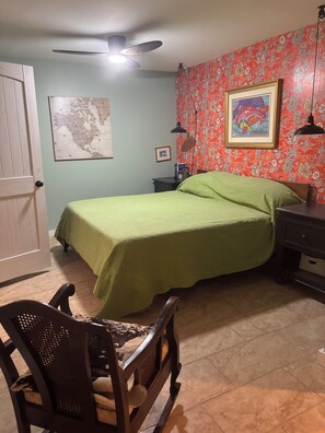 Ein Schlafzimmer mit einem Bett, einem Sessel, einem Schreibtisch, einer Karte und einem Deckenventilator.