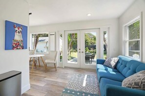 Un salon moderne avec un canapé bleu, un tapis à motifs et un coin repas comprenant une table et des chaises blanches.