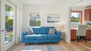 Een moderne woonkamer met een blauwe bank, een eethoek met een houten tafel en een keuken met houten keukenkastjes.